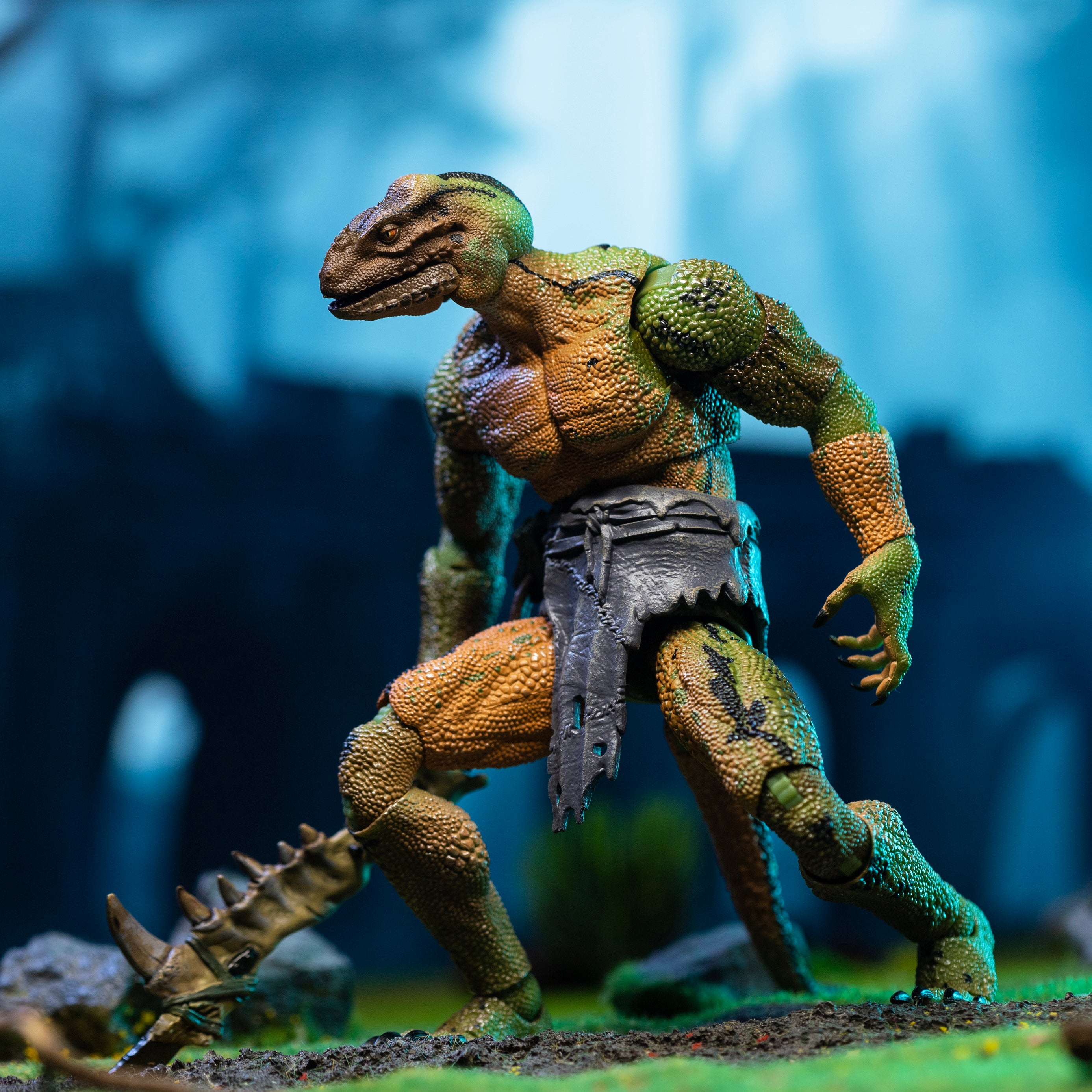 Green, yellow, and black Lemurian in loin cloth crouching and holding mandible club at hip height in right hand.